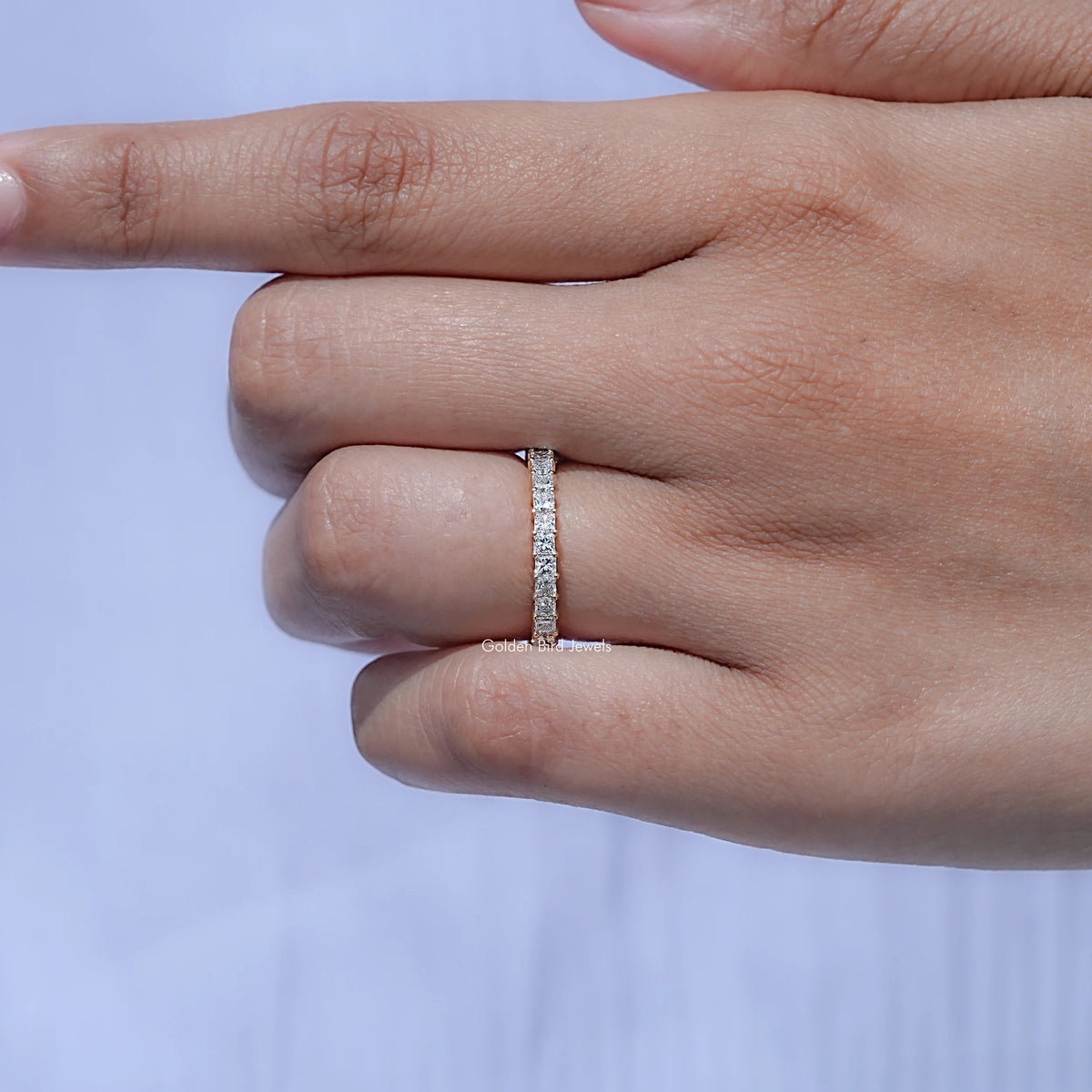 Slim silver diamond eternity ring on hand, square-cut stones around the band