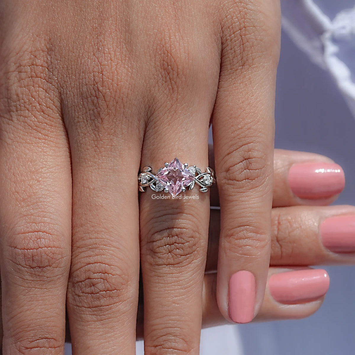 Pink lab gemstone leaf engagement ring on finger with silver band and small sparkle stones