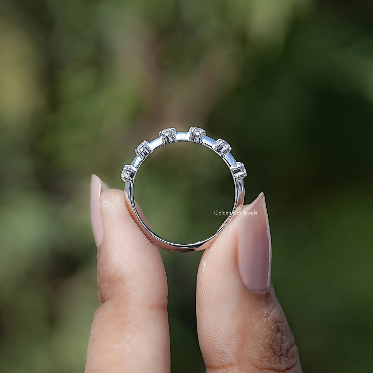 Silver half eternity band with princess-cut stones, held up to show circle