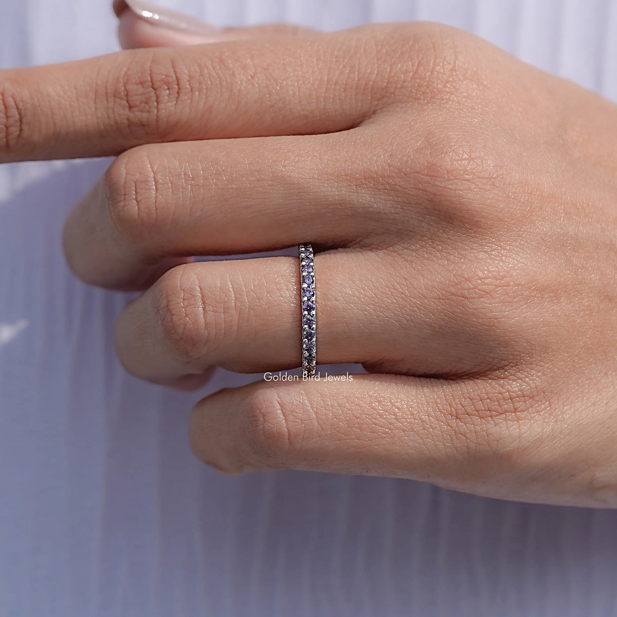 Silver amethyst eternity band ring with purple round stones, worn on hand