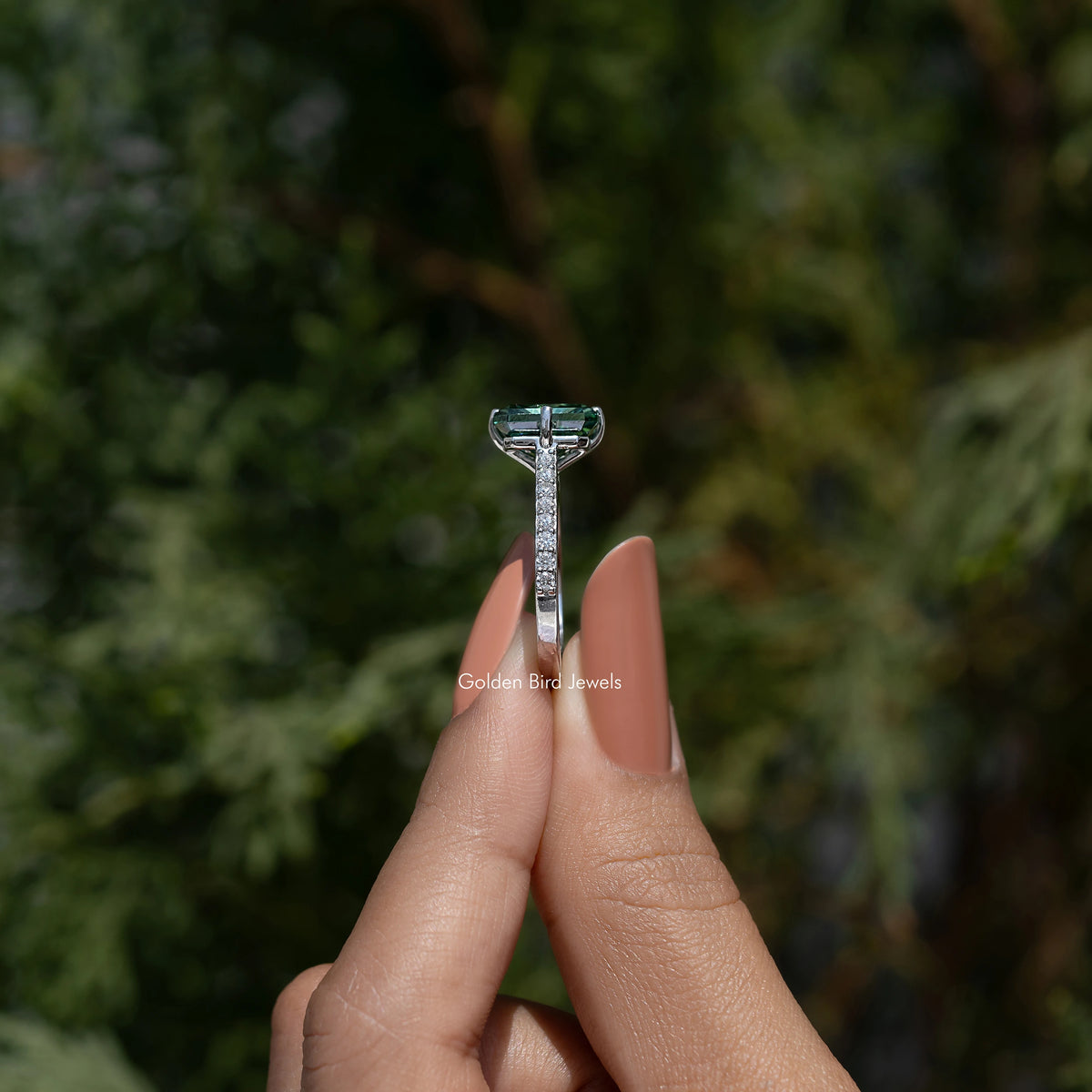 Top view of green emerald-cut solitaire ring with prong-set center and halo-like side detailing