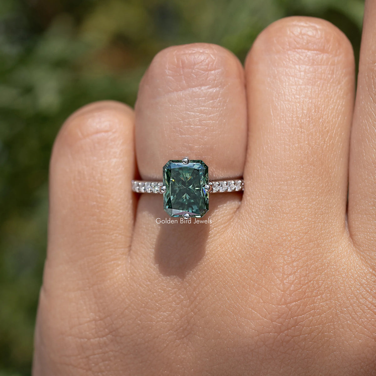 Green emerald-cut solitaire ring with sparkling side stones on a slim band