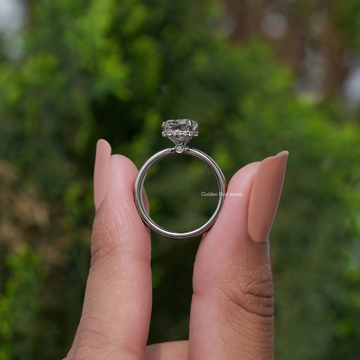 Square-cut diamond halo ring on a silver band, held between fingers