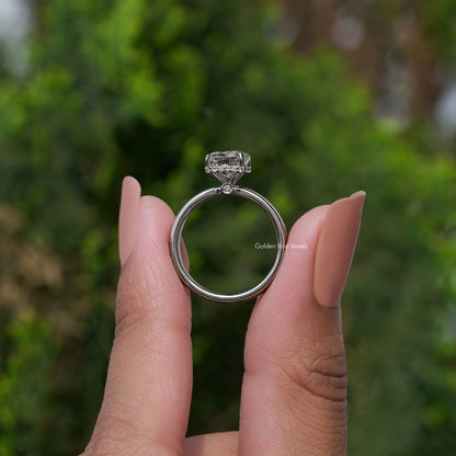 Square-cut diamond halo ring on a silver band, held between fingers