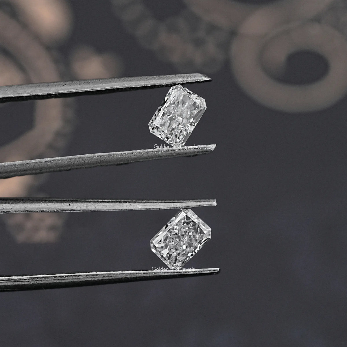 Radiant-cut loose diamonds, two clear stones held between metal tweezers.
