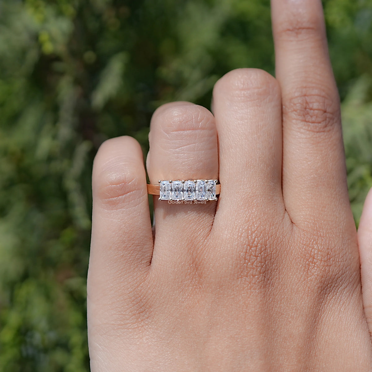 Five-stone moissanite radiant-cut ring on finger, clear stones across the band