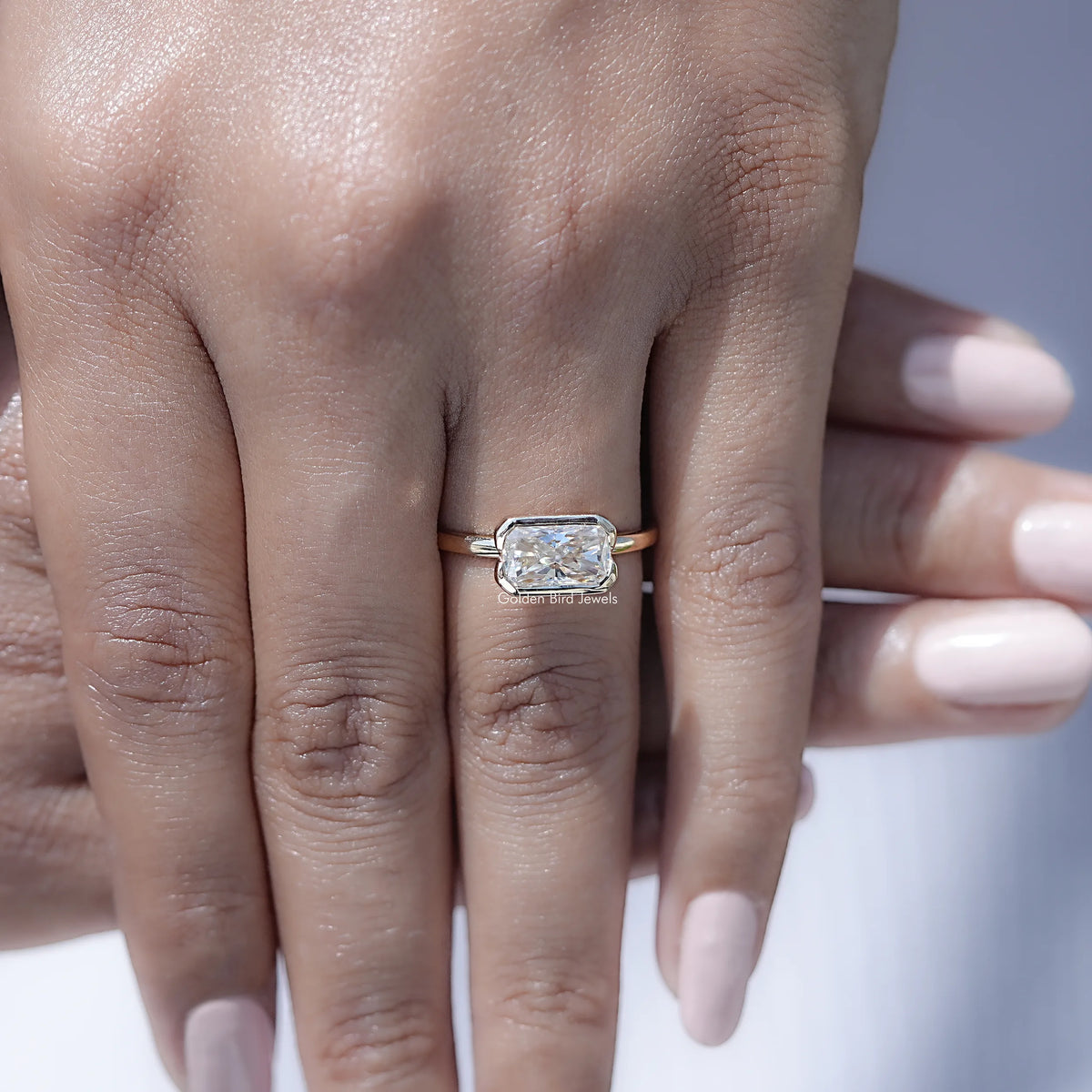 Radiant-cut moissanite solitaire ring with half bezel setting, worn on hand