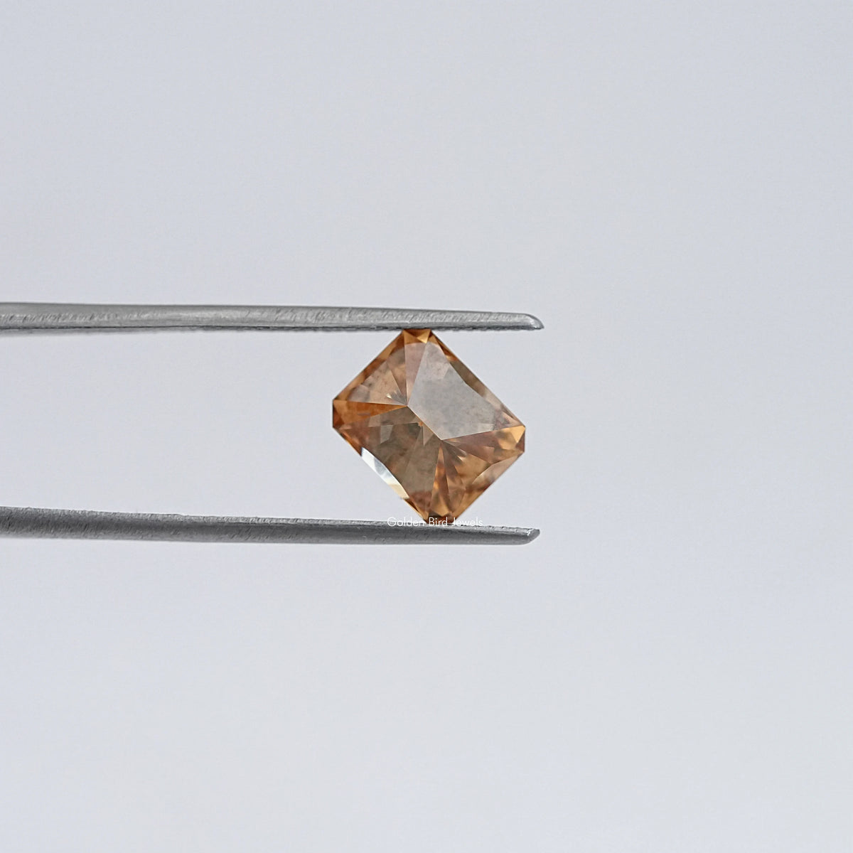 Emerald-cut champagne moissanite loose stone held in metal tweezers