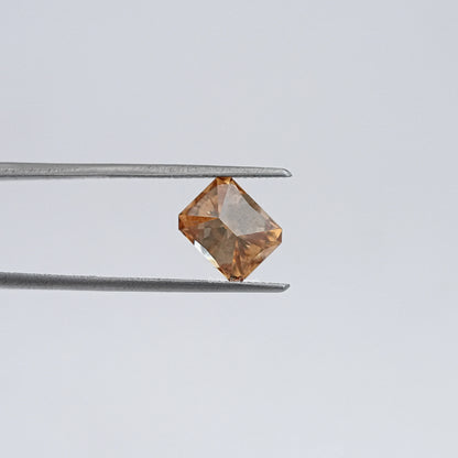 Emerald-cut champagne moissanite loose stone held in metal tweezers