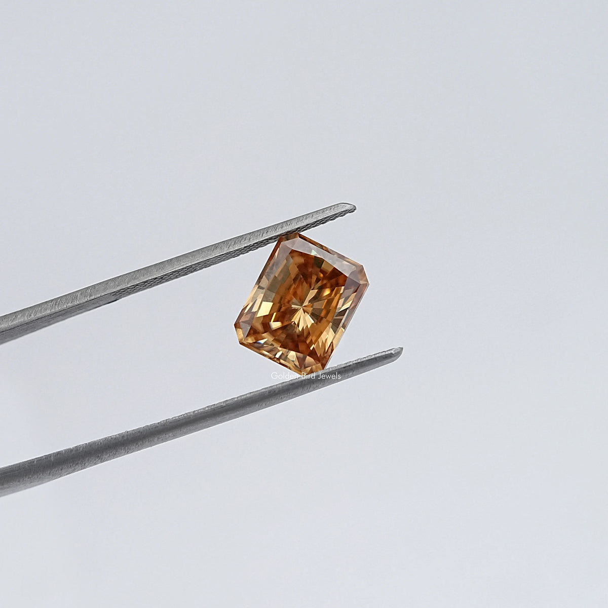 Emerald-cut champagne moissanite loose stone in tweezers, angled view