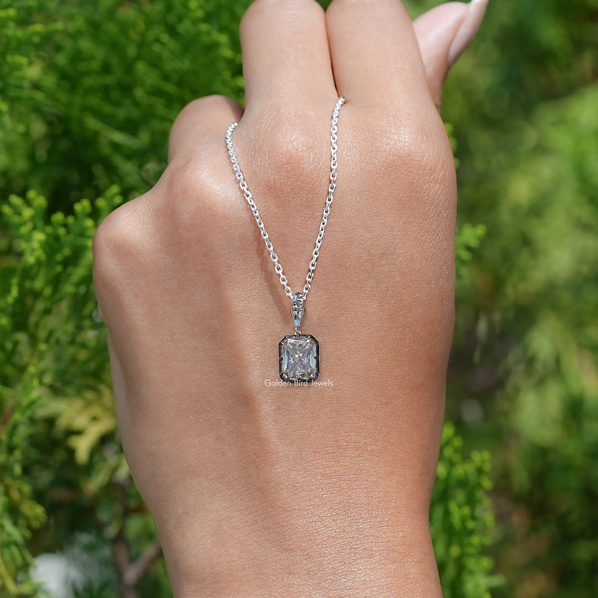 Square-cut moissanite solitaire pendant with silver chain on open palm