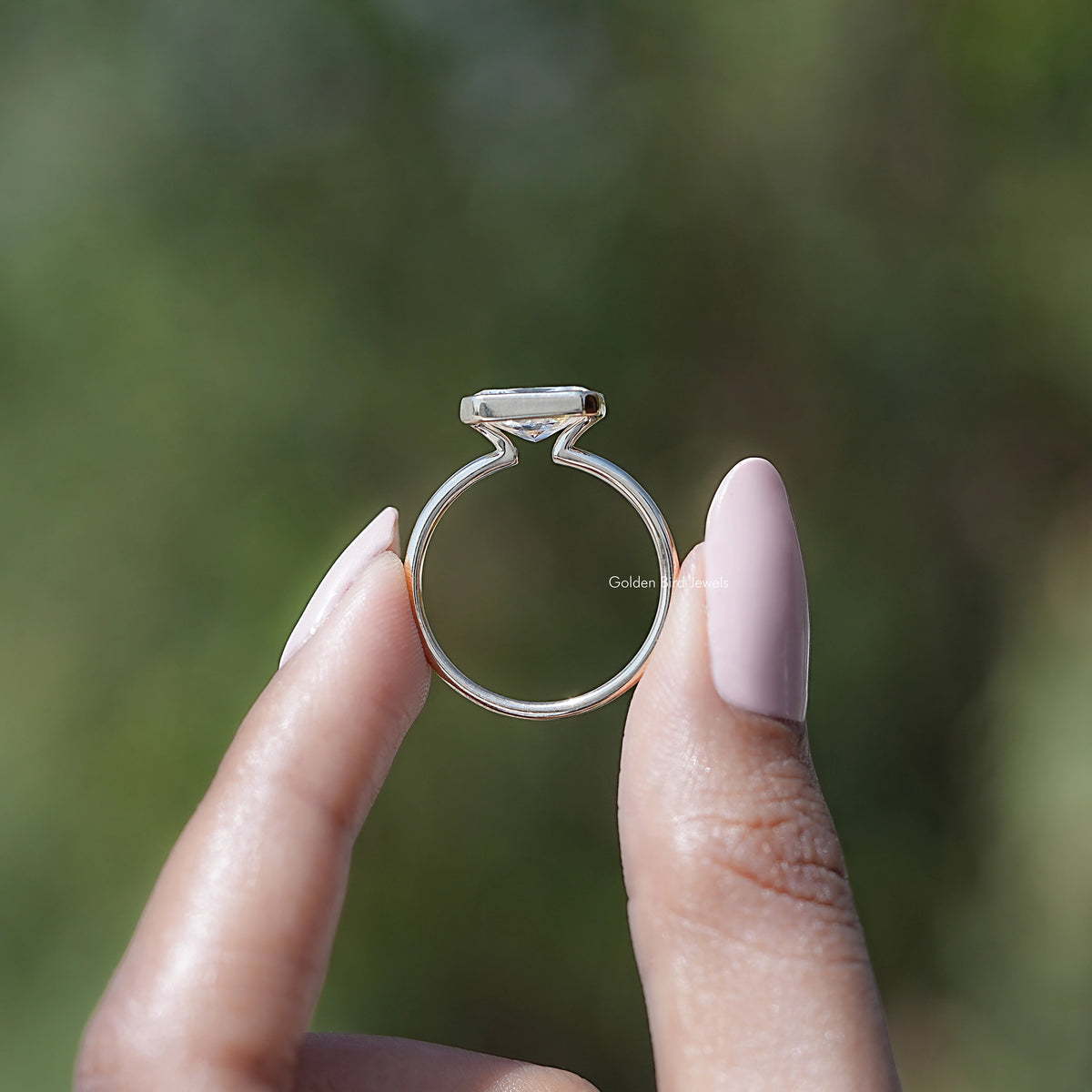 Profile view of gold-toned solitaire ring with radiant-cut stone and half bezel