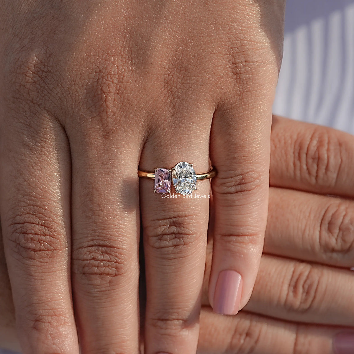 Two-stone oval diamond and pink gemstone ring on hand, rose gold-tone band