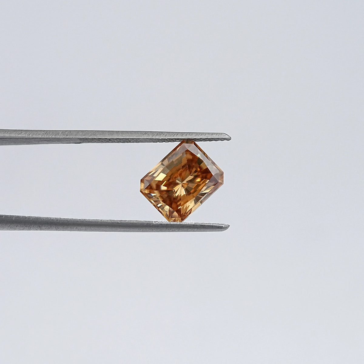 Emerald-cut champagne moissanite loose stone, held in tweezers angled view
