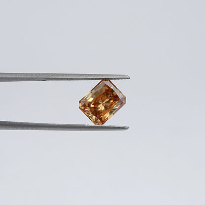 Emerald-cut champagne moissanite loose stone, held in tweezers angled view