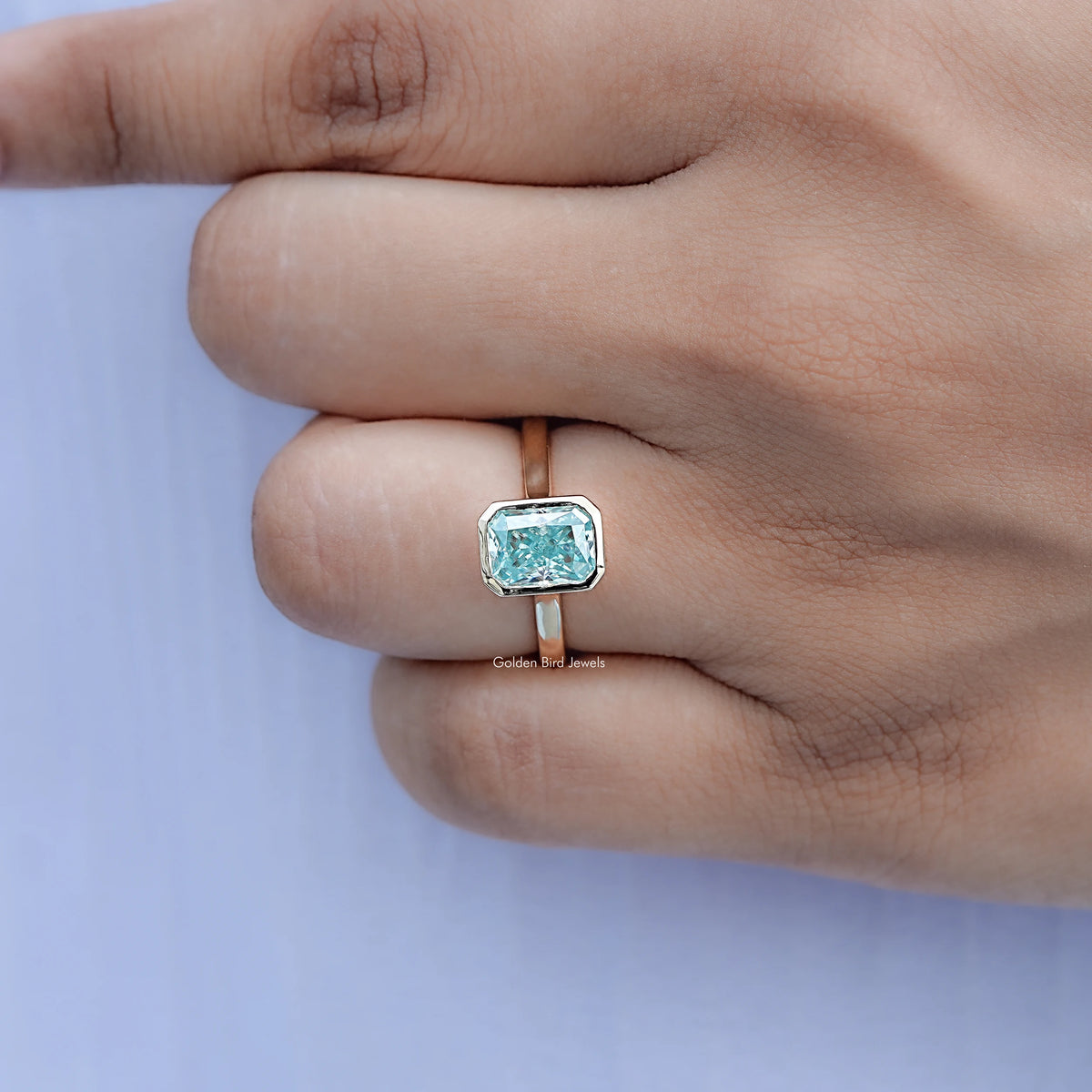 Blue moissanite bezel solitaire ring on finger with squared blue center stone