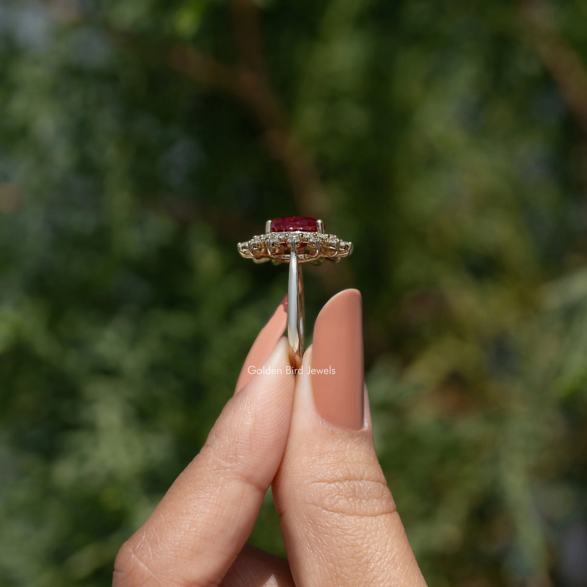 Side profile of oval halo engagement ring with red center stone, held on hand