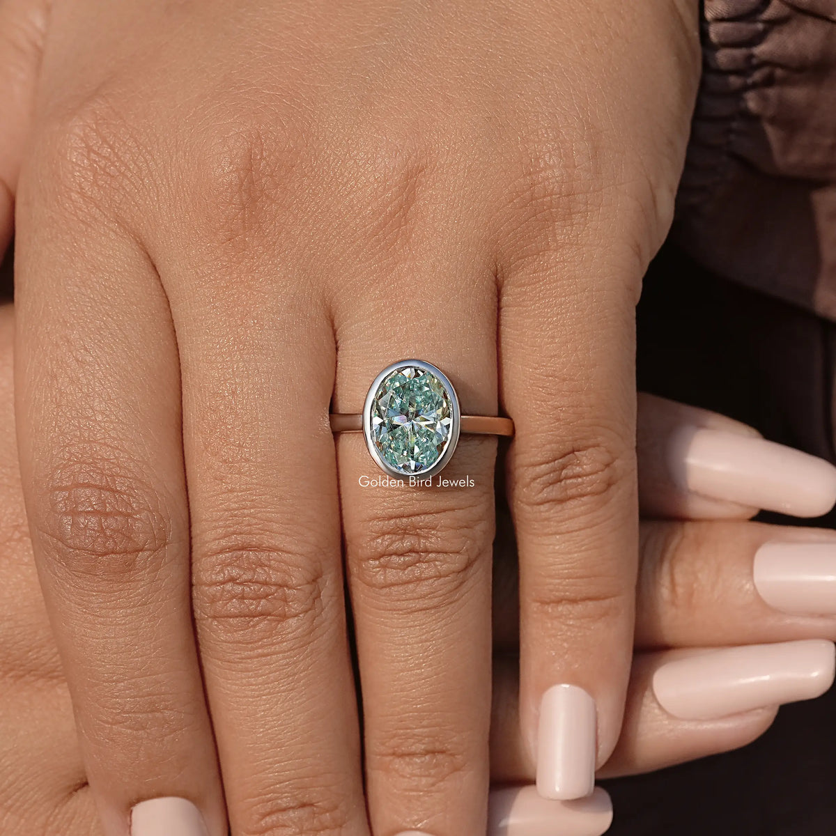 Gold-tone oval moissanite bezel-set solitaire engagement ring on hand