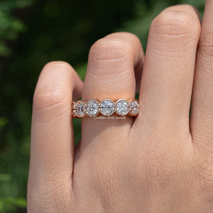 Rose-gold tone bezel-set round diamond wedding band seen from an angled view