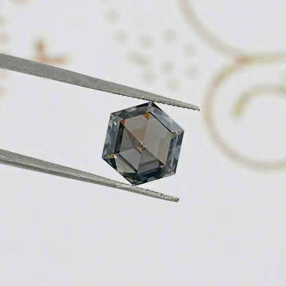 Hexagon-cut gray moissanite gemstone held by tweezers, reflective faceted crown