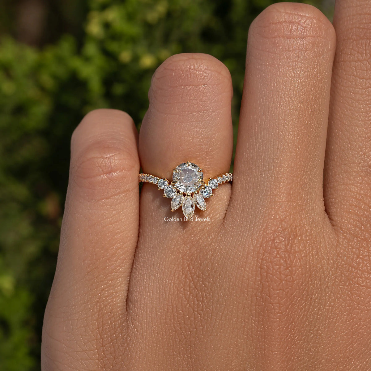 Gold-tone curved engagement ring on hand, round center stone with marquise accents