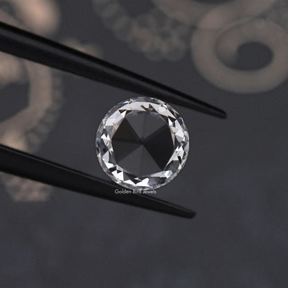 Round rose-cut lab-grown diamond close-up between two black prongs, tilted angle