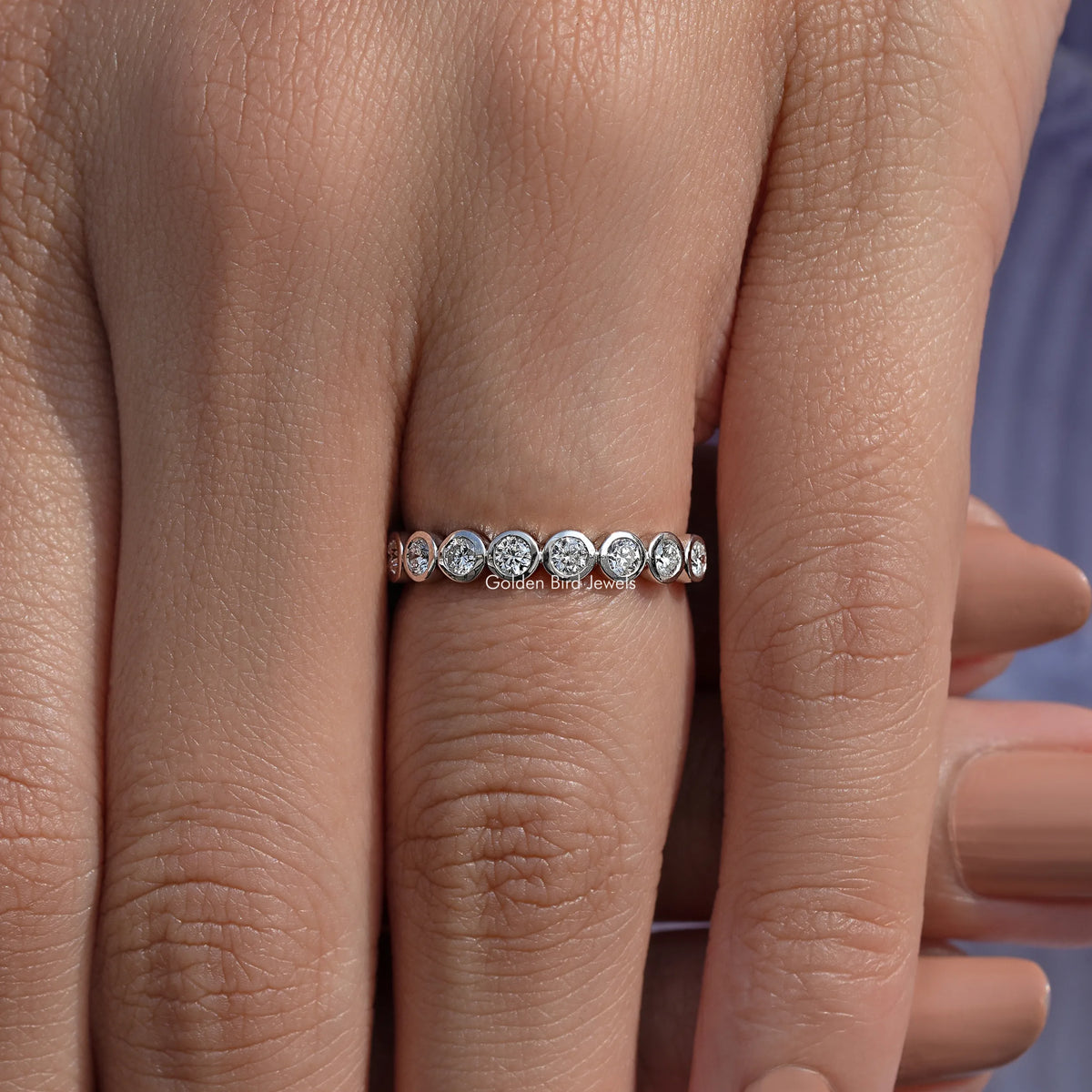 Silver-toned round bezel lab diamond wedding band on hand, slim row of stones