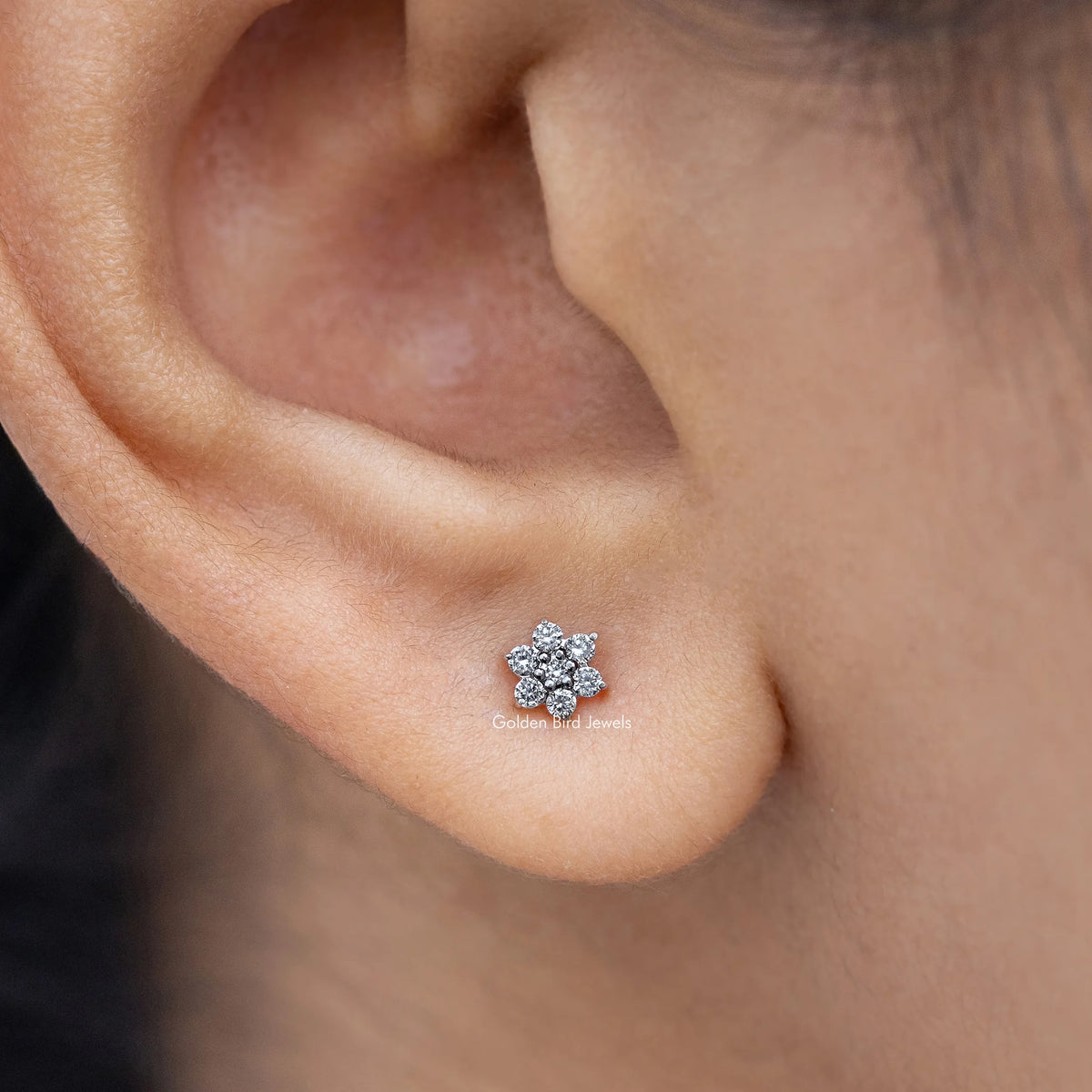 Floral-shaped diamond stud earring close-up, round cluster of clear stones in silver.