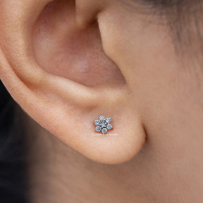 Floral-shaped diamond stud earring close-up, round cluster of clear stones in silver.