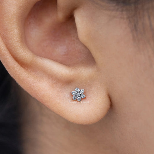Floral-shaped diamond stud earring close-up, round cluster of clear stones in silver.