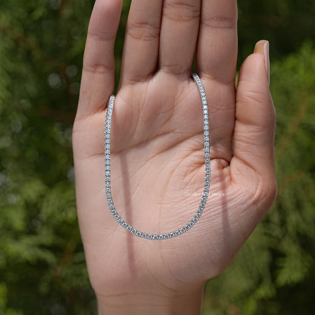 Lab-grown diamond tennis necklace with round-cut stones held in open palm, teardrop drape