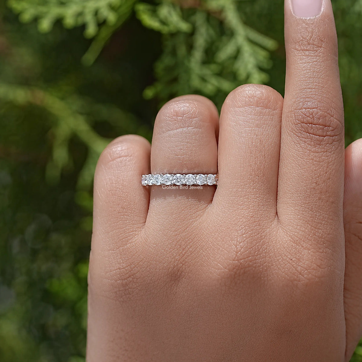 Half eternity moissanite ring with a row of clear round-cut stones, on finger