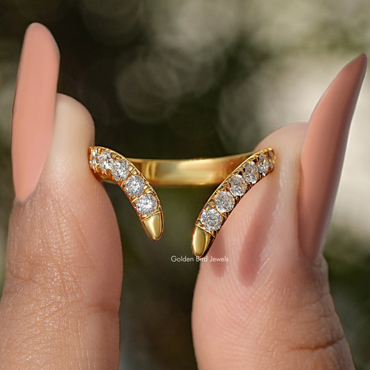 Gold open V-shape wedding band with round-cut stones, front view between fingers