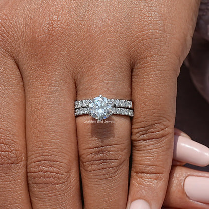 Moissanite engagement ring set with round center stone and pavé bands on a finger