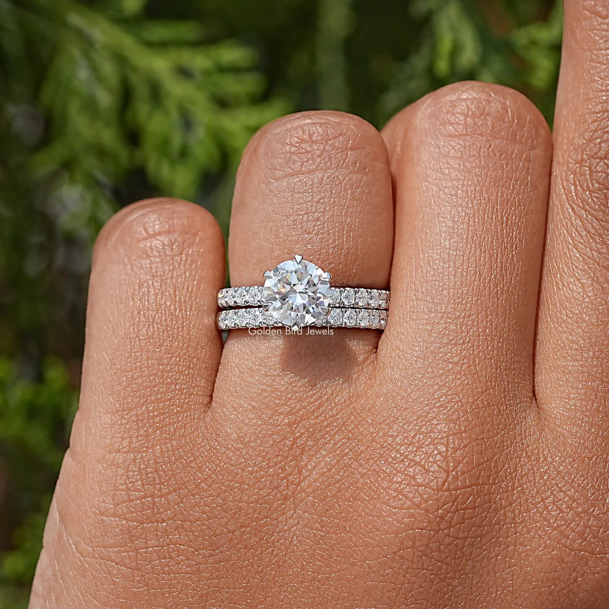 Round moissanite engagement ring set with pavé bands on a hand