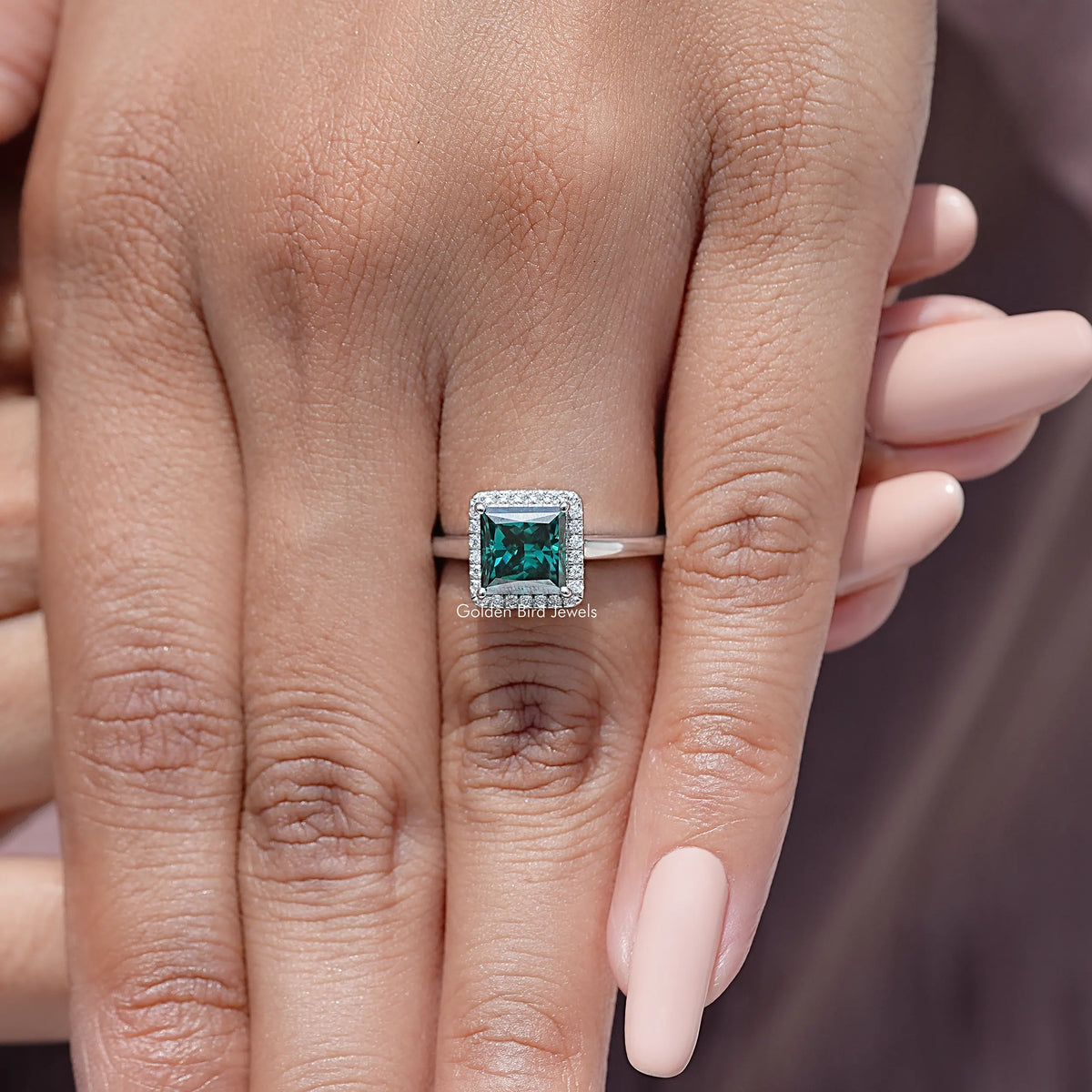 Square teal moissanite engagement ring with halo border, worn on hand