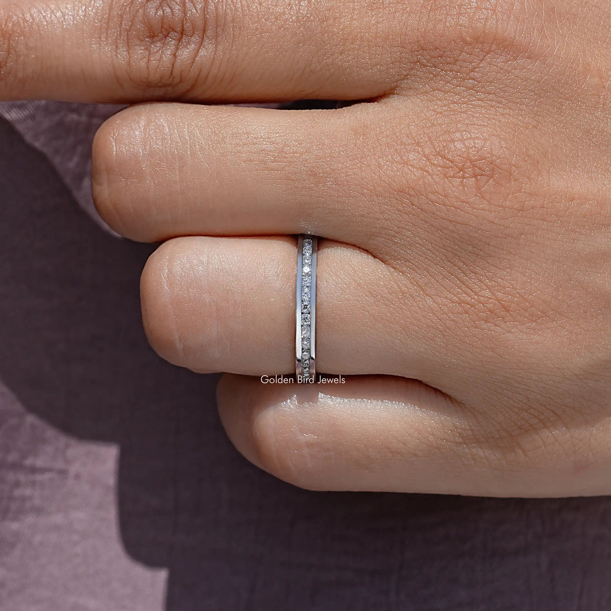 Moissanite eternity band with channel-set round stones on finger, silver-tone metal