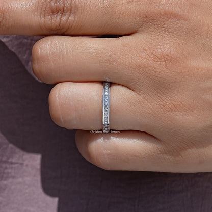 Moissanite eternity band with channel-set round stones on finger, silver-tone metal