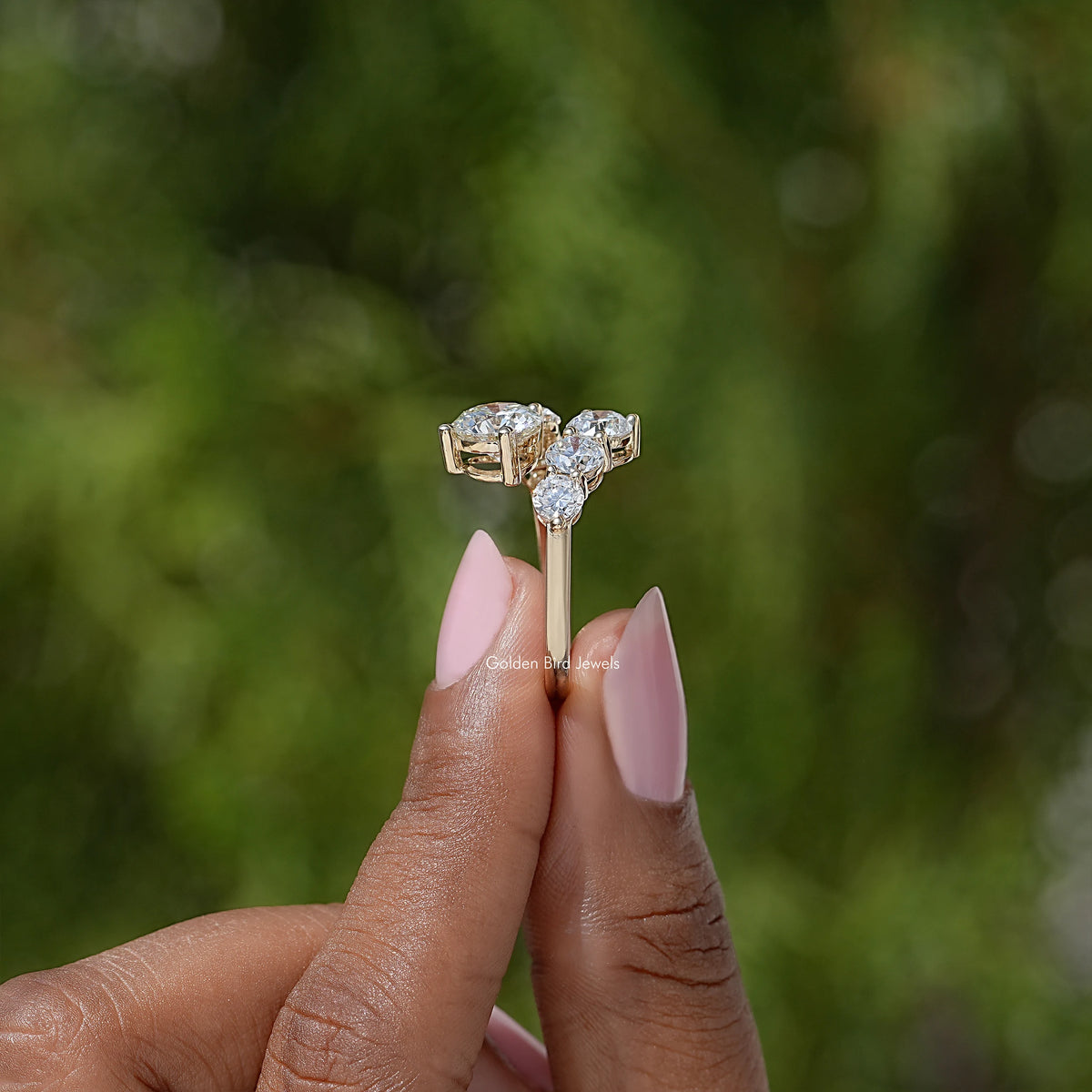 Close-up of a round-cut moissanite bypass ring with three stones on fingertip