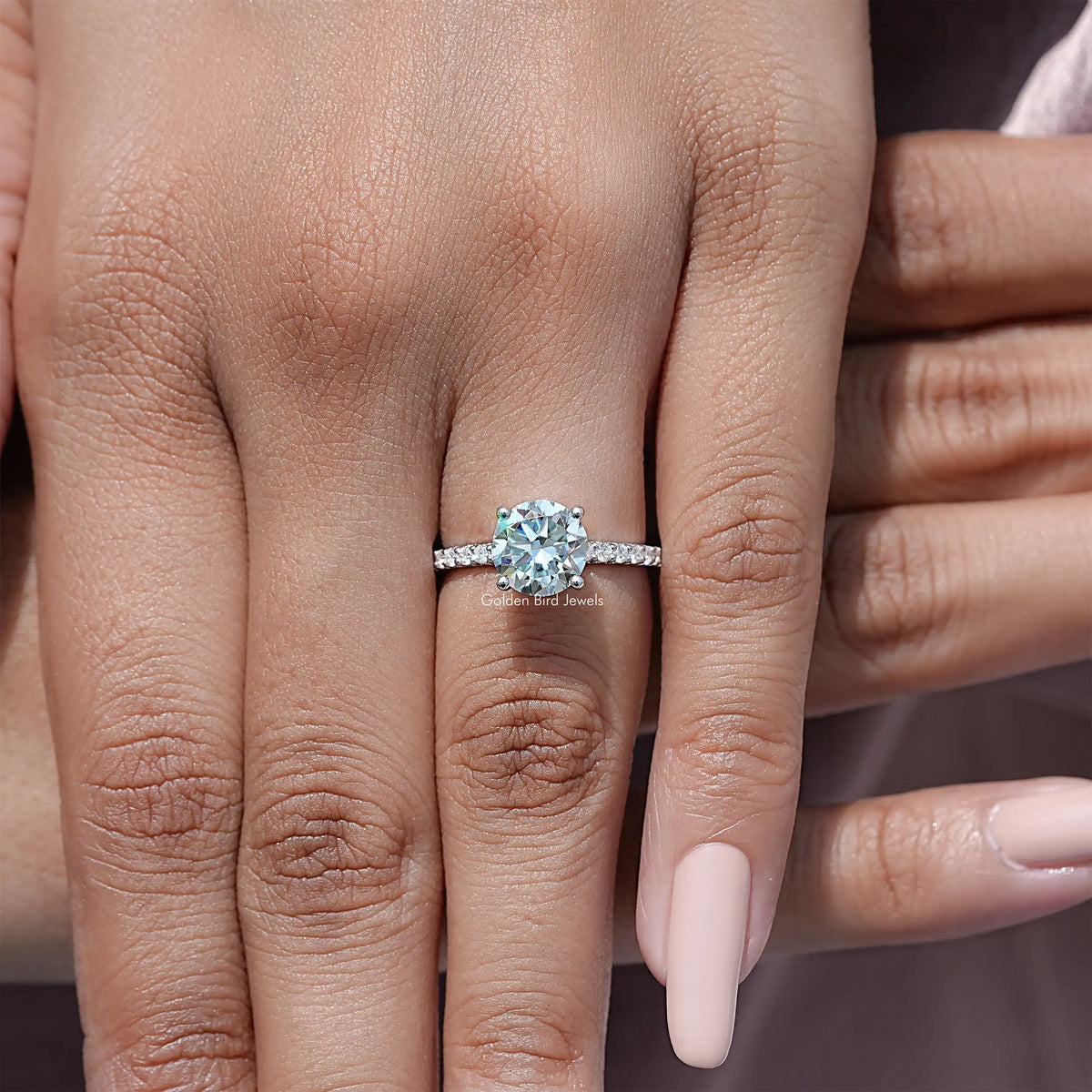 Round-cut moissanite solitaire accent ring with pavé band on a finger