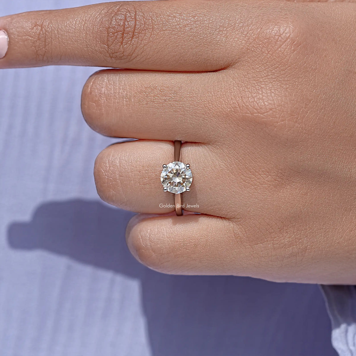 Sterling silver solitaire ring with round moissanite stone, close-up on finger