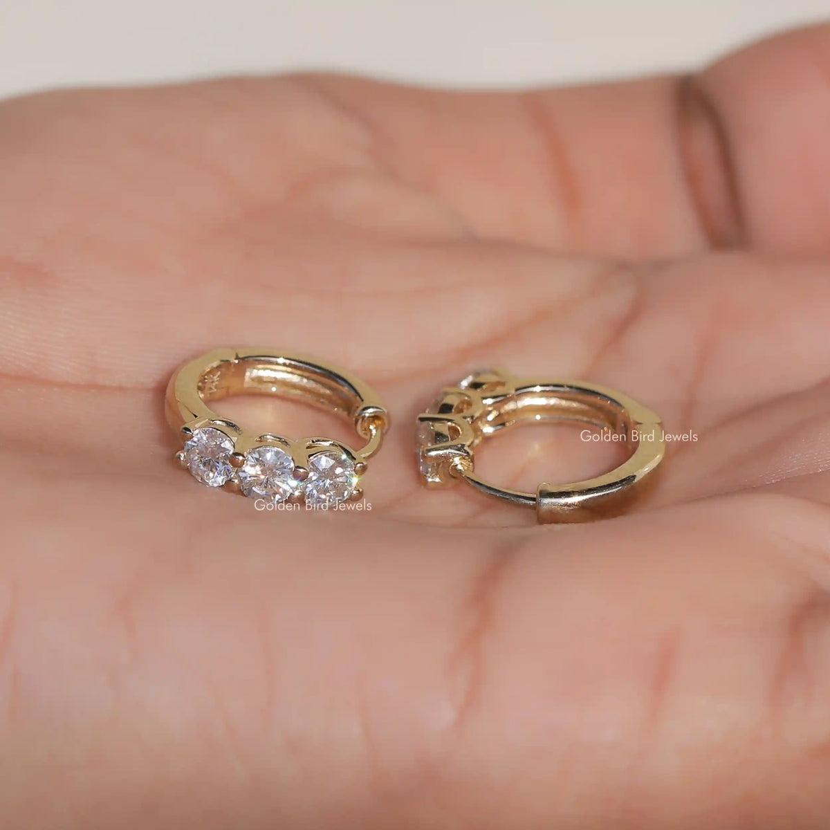 Gold-tone huggie hoop earrings with three round-cut stones, close-up on open palms