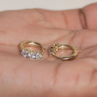 Gold-tone huggie hoop earrings with three round-cut stones, close-up on open palms