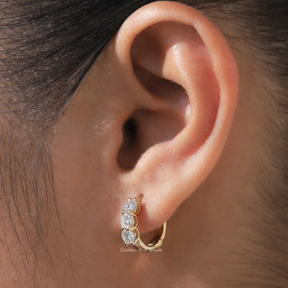 Silver-tone huggie hoop earrings with three round-cut stones, close-up on ear
