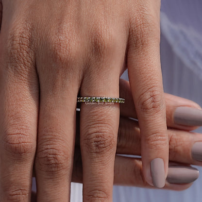 Green eternity band ring on finger, row of round stones across the band
