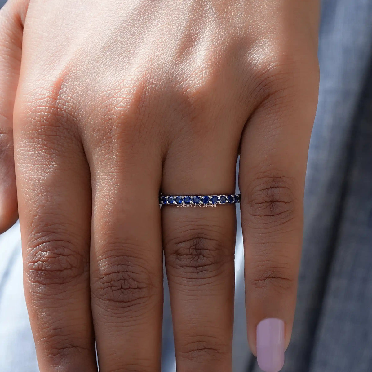 In finger front view of September Birthstone Sapphire Blue Round Eternity Band in unique shape
