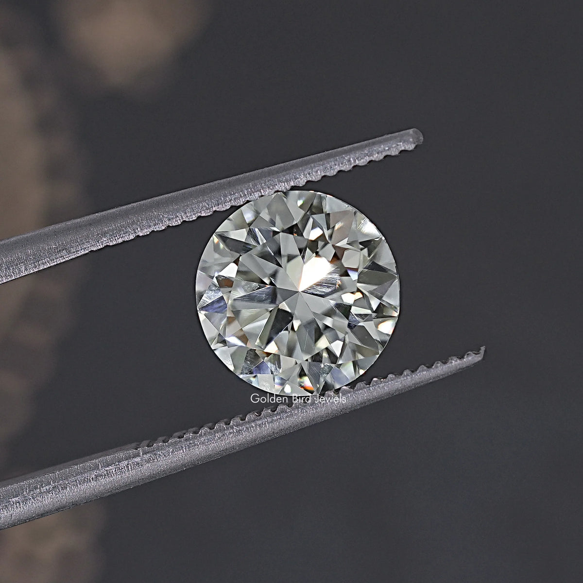 Round moissanite loose stone in silver tweezers, round brilliant facets, clear.
