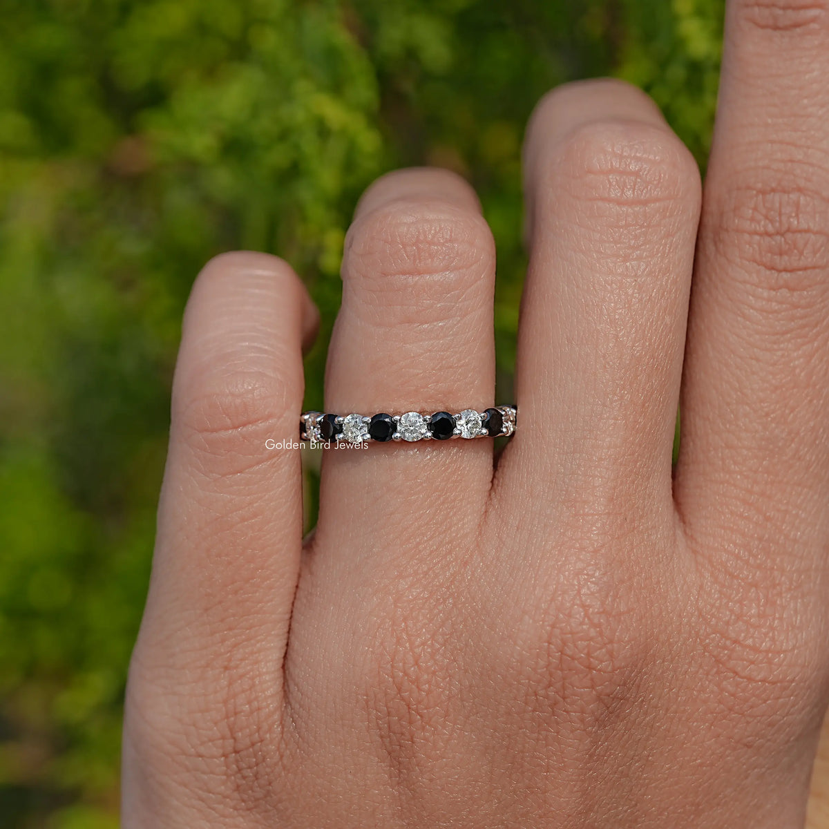 Silver eternity ring with alternating round clear and dark stones on finger