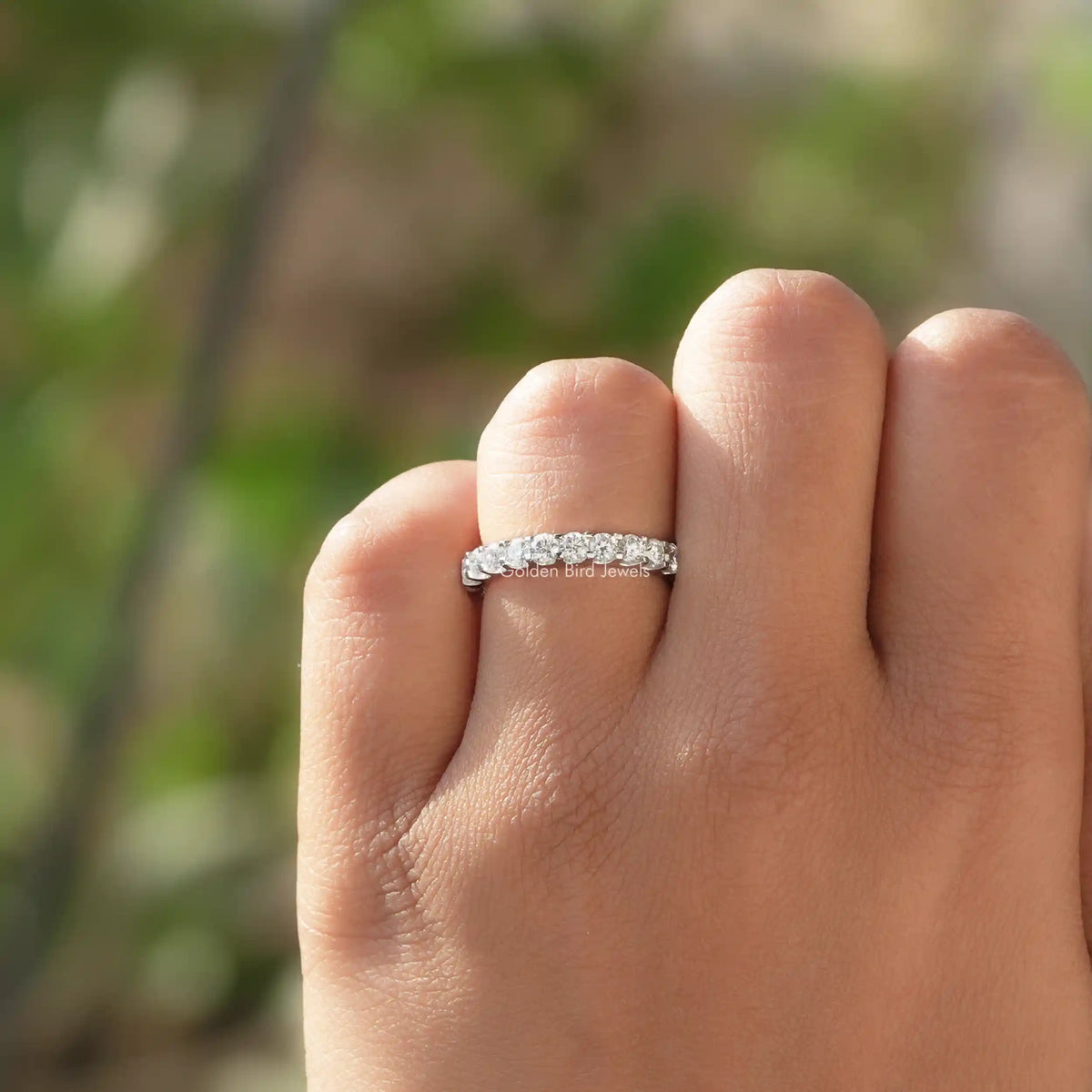 Round moissanite full eternity wedding band on finger, silver-toned with evenly spaced round stones