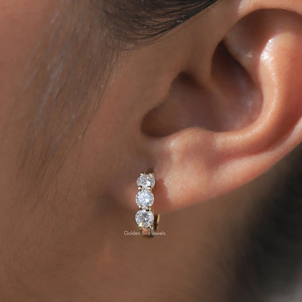 Silver-tone huggie hoop earrings with three round-cut sparkling stones, side view on ear